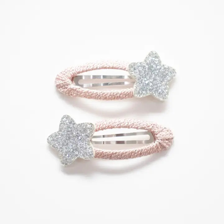 Photo of two kids’ hair clips with silver glitter star accents attached to soft blush-pink oval bases, displayed on a white card with a small gold heart.