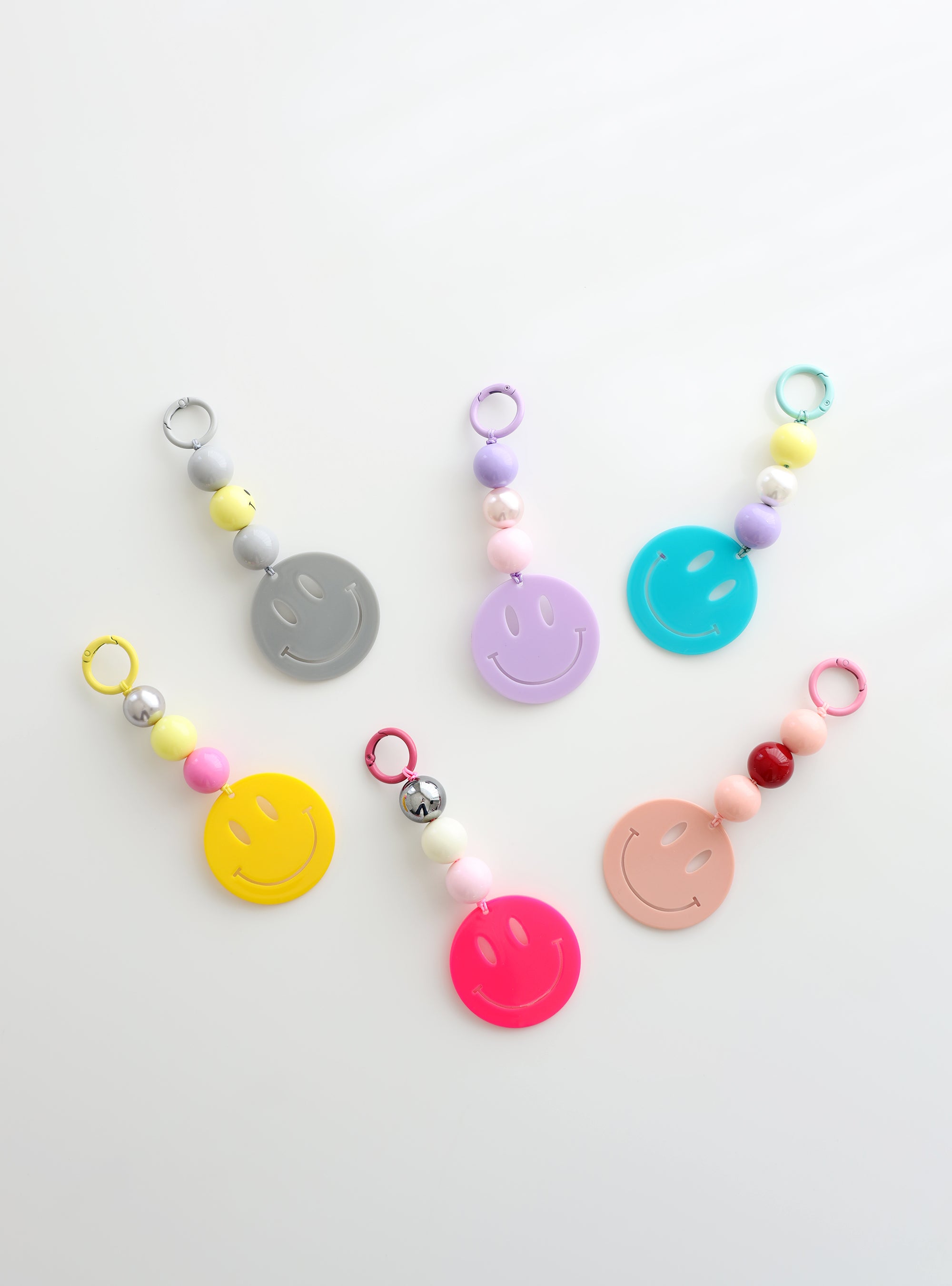 Six colorful smiley face keychains with playful bead accents in pastel and bold shades, displayed on a white surface.