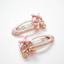Two pink hair clips decorated with glitter ballet shoes and pink bows on a woven oval base.