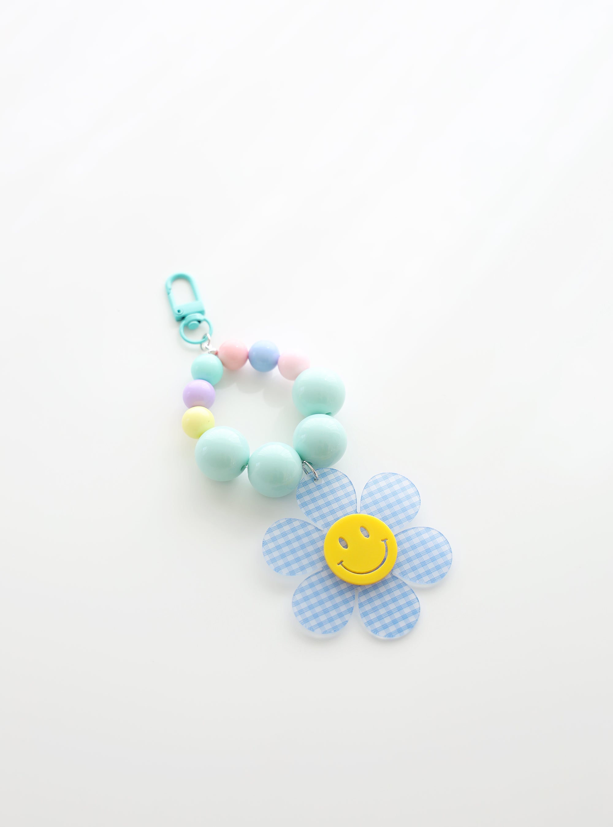 A beaded keychain featuring bright soft sky blue beads and pastel accents, with a soft sky blue gingham flower charm and a cheerful yellow smiley face center, attached to a soft sky blue clasp.