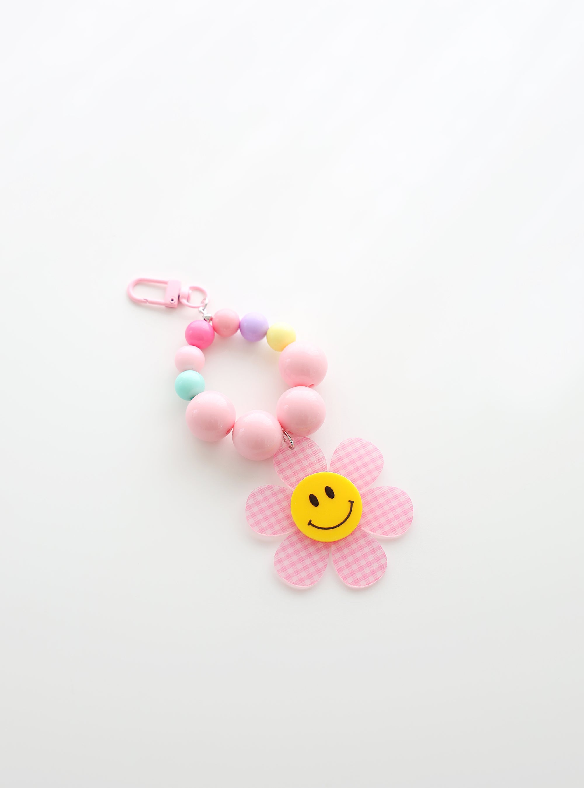 A beaded keychain featuring bright soft pink beads and pastel accents, with a soft pink gingham flower charm and a cheerful yellow smiley face center, attached to a soft pink clasp.