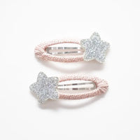 Photo of two kids’ hair clips with silver glitter star accents attached to soft blush-pink oval bases, displayed on a white card with a small gold heart.
