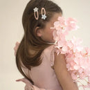 Young girl wearing a pink dress with two silver glitter star hair clips on her side part, holding soft pink flowers.