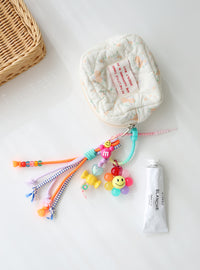 Colorful bag charms with beads and a smiley flower attached to a white pouch.