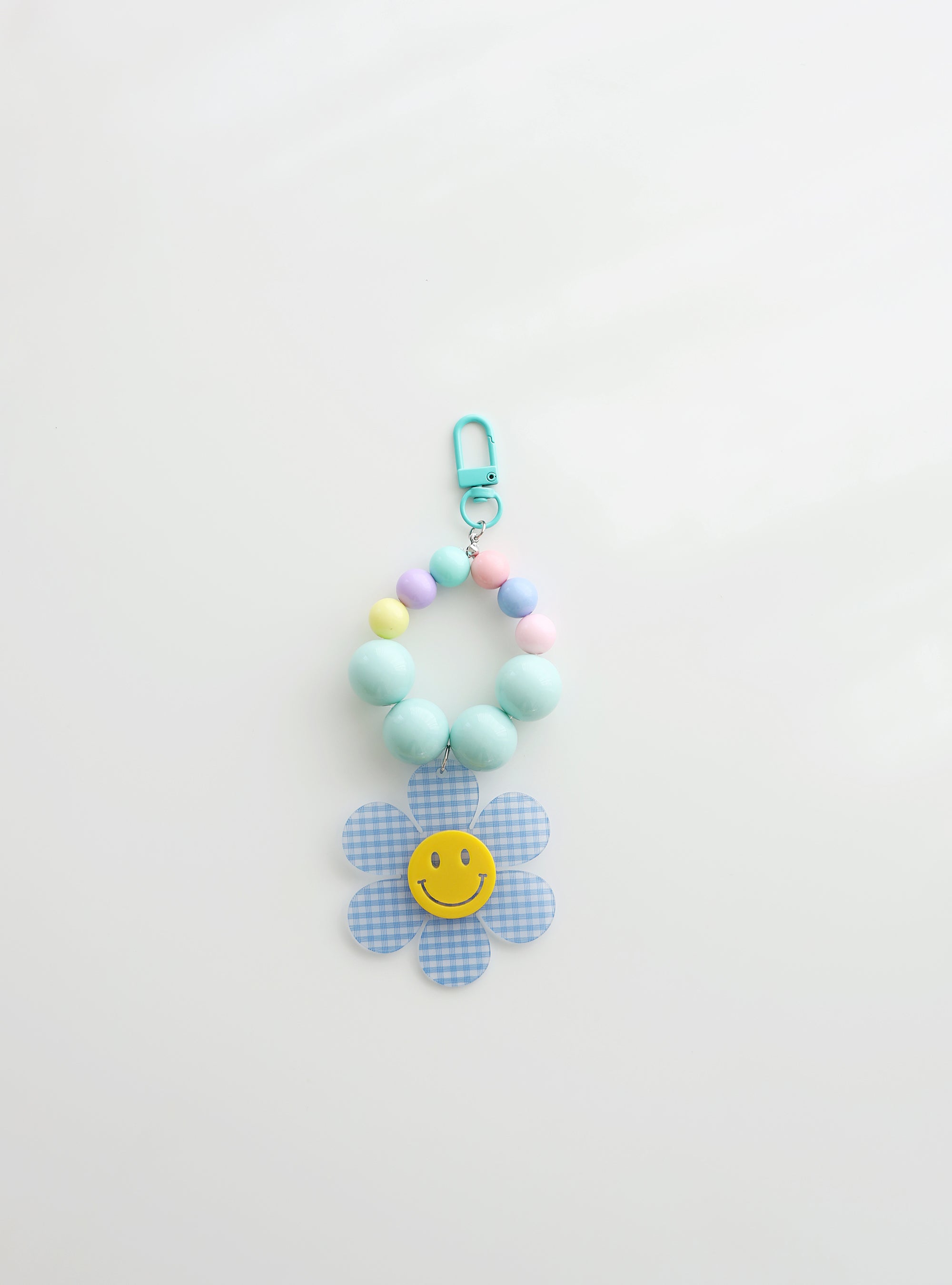 A beaded keychain featuring bright soft sky blue beads and pastel accents, with a soft sky blue gingham flower charm and a cheerful yellow smiley face center, attached to a soft sky blue clasp.