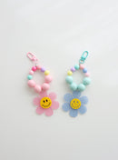Two colorful beaded keychains with gingham flower smiley charms — one in pink and one in sky blue — on a white background.