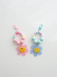 Two colorful beaded keychains with gingham flower smiley charms — one in pink and one in sky blue — on a white background.