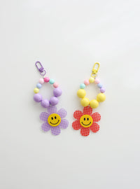 Two colorful beaded keychains with gingham flower smiley charms — one in soft purple and one in red — on a white background.