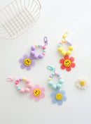 Four colorful beaded keychains with large pastel beads and playful gingham flower charms featuring smiley faces, displayed on a white background with white basket and a daisy decoration.