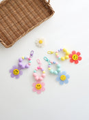 Four colorful beaded keychains with large pastel beads and playful gingham flower charms featuring smiley faces, displayed on a white background with basket and a daisy decoration.