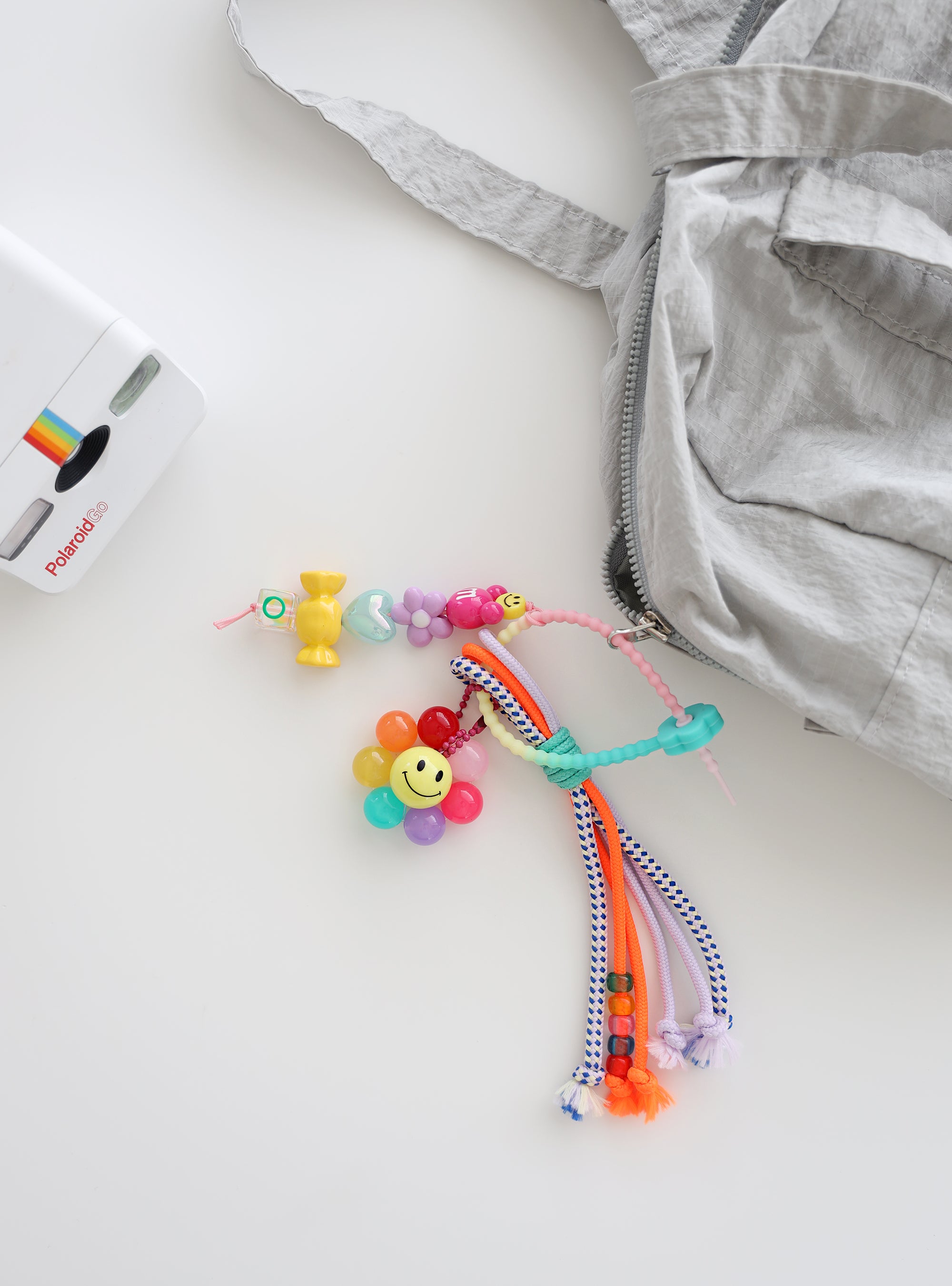 Colorful bag charms with beads and a smiley flower attached to a light gray fabric tote bag.