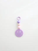 A lavender smiley face keychain with three round beads in lavender, pearl white, and soft pink, displayed against a clean white background.