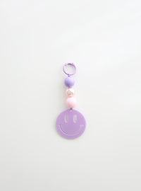 A lavender smiley face keychain with three round beads in lavender, pearl white, and soft pink, displayed against a clean white background.
