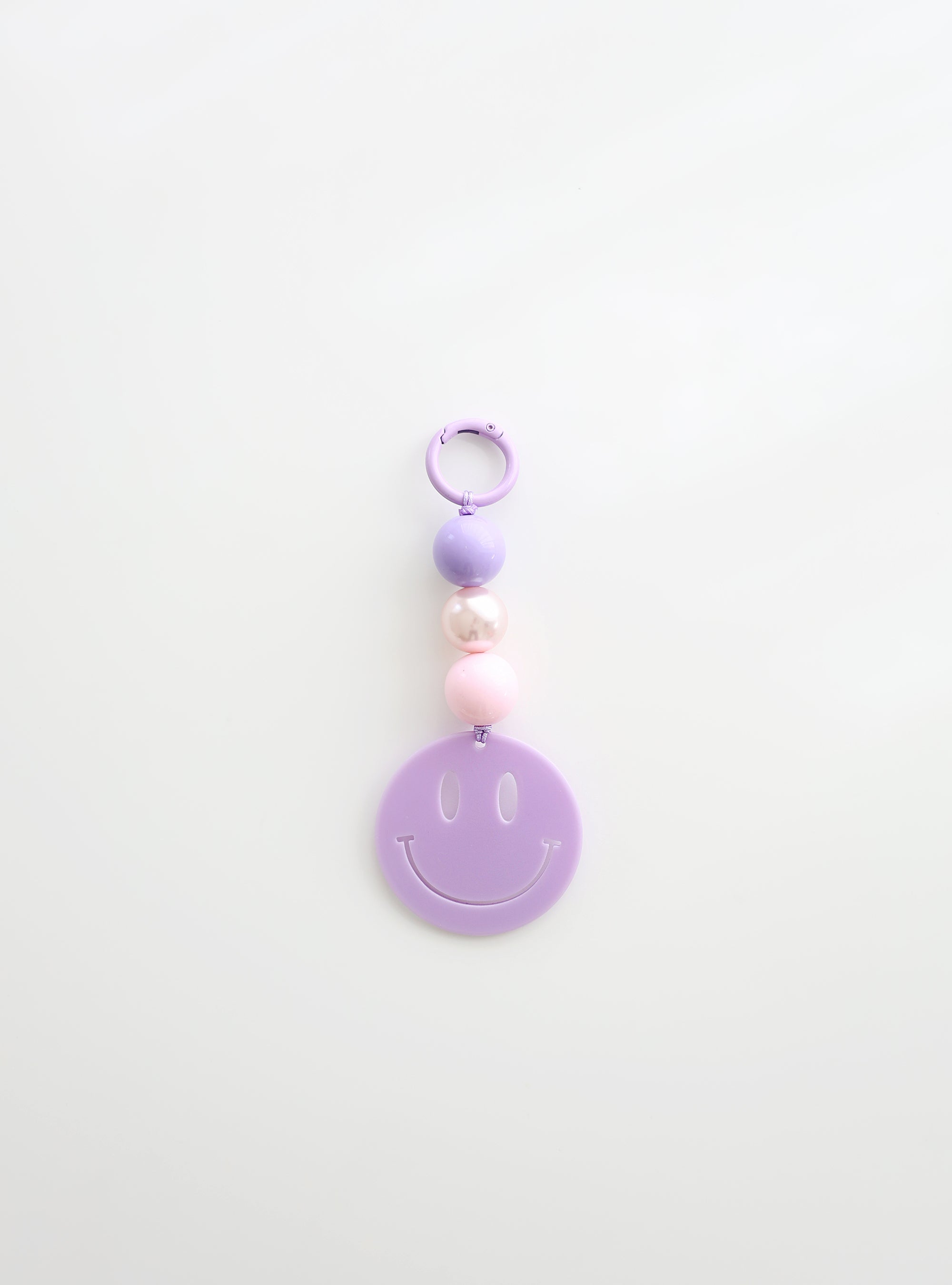 A lavender smiley face keychain with three round beads in lavender, pearl white, and soft pink, displayed against a clean white background.