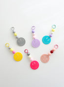 Six colorful smiley face keychains with playful bead accents in pastel and bold shades, displayed on a white surface.
