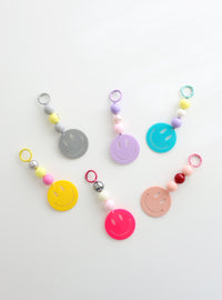 Six colorful smiley face keychains with playful bead accents in pastel and bold shades, displayed on a white surface.