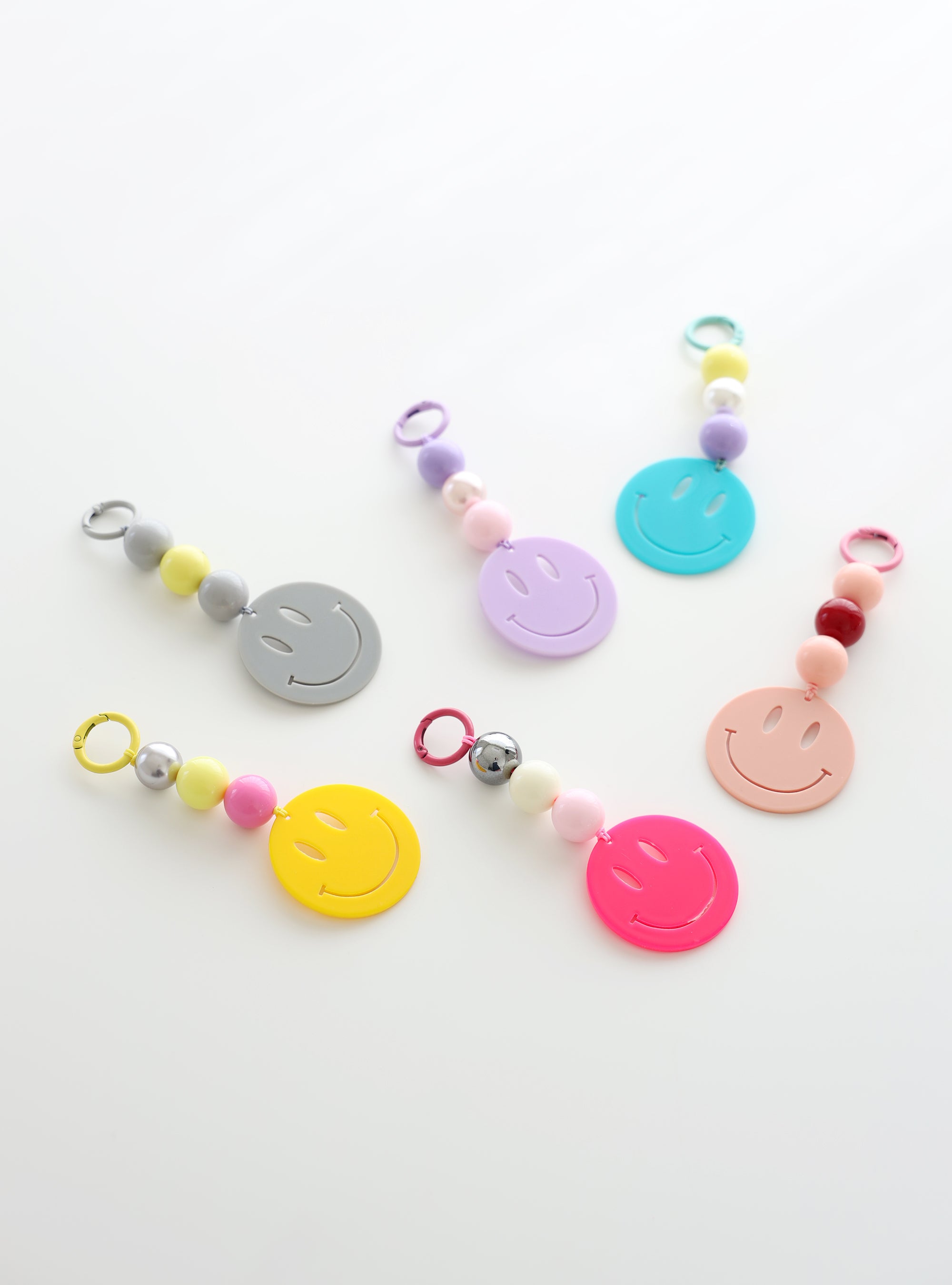 Six colorful smiley face keychains with playful bead accents in pastel and bold shades, displayed on a white surface.