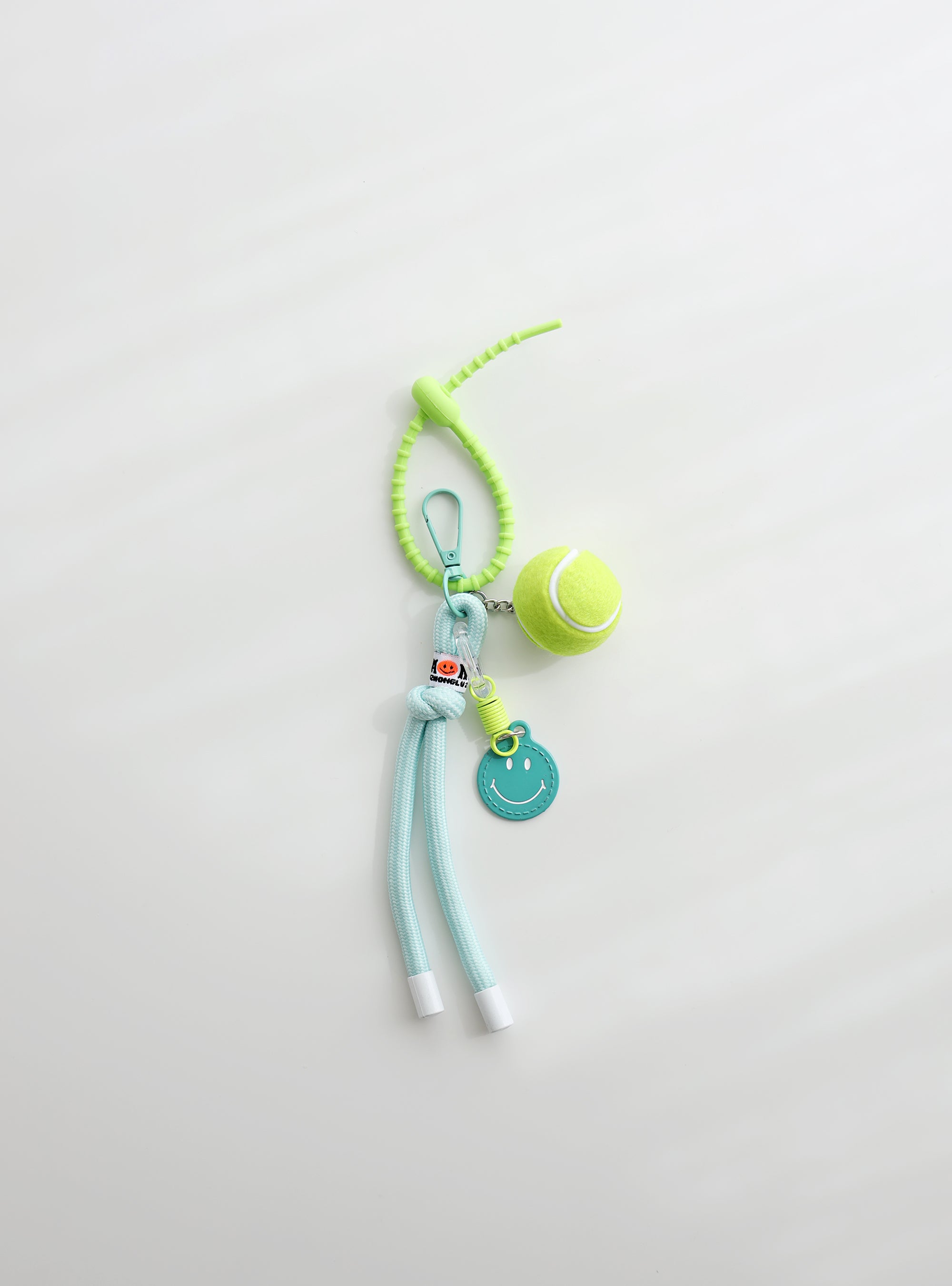 A bright green tennis ball keychain featuring a mini tennis ball charm, a mint smiley face tag, and an adjustable loop strap for easy attachment, displayed on a clean white background.