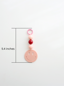 One colorful smiley face keychain, in pink, featuring round pastel beads and a large smiley face charm, showing its measurement of length, 5.4inches on a white background.