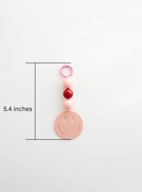 One colorful smiley face keychain, in pink, featuring round pastel beads and a large smiley face charm, showing its measurement of length, 5.4inches on a white background.
