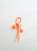 A bright orange tennis ball keychain featuring a mini tennis ball charm, a orange smiley face tag, and an adjustable loop strap for easy attachment, displayed on a clean white background.