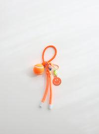 A bright orange tennis ball keychain featuring a mini tennis ball charm, a orange smiley face tag, and an adjustable loop strap for easy attachment, displayed on a clean white background.