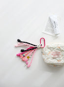 A playful multi-rope keychain featuring knotted cords in pink, black, and white with colorful beads and a small yellow smiley charm, attached to a pink clasp and shown clipped to a quilted pouch on a white background.