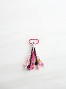 A playful multi-rope keychain featuring knotted cords in pink, black, and white with colorful beads and a small yellow smiley charm, attached to a pink clasp on a white background.