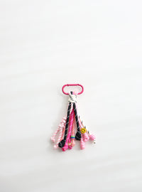 A playful multi-rope keychain featuring knotted cords in pink, black, and white with colorful beads and a small yellow smiley charm, attached to a pink clasp on a white background.