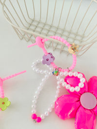 Neon pink five-petal flower bag charm with a light pink center, pearl bead bow, and pink silicone clasp. Clasp has small clips in various shapes and colors, shown here as a purple flower and beige crown.