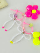 Two bag charms with pearl bead bows and silicone clasps. One has a neon pink flower with a yellow center, and the other has a neon yellow flower with a pink center. Clasp clips vary in shape and color, shown here as a purple flower and a green flower.