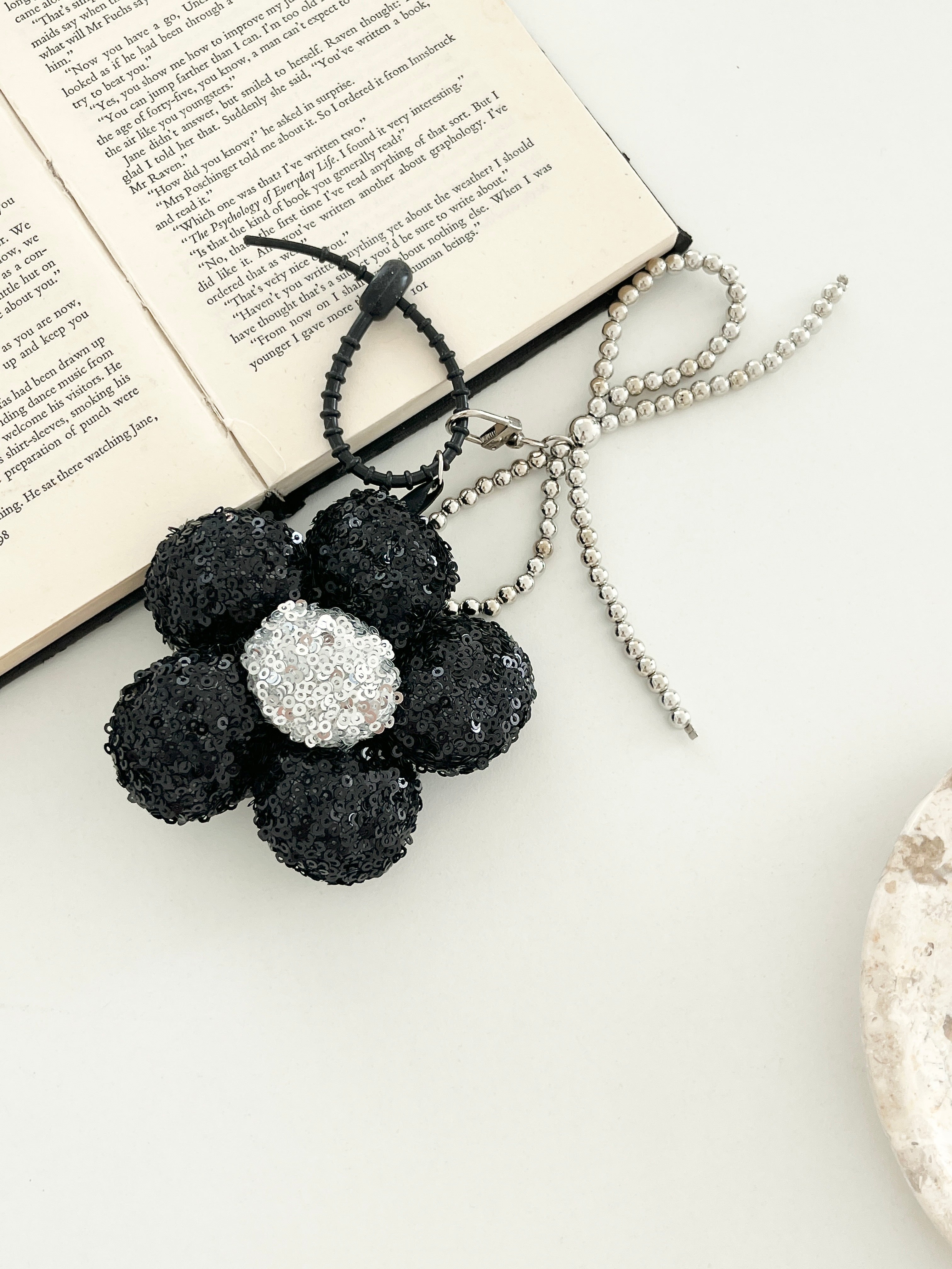 One black sequined flower keychains, with a silver center shown on an open book.