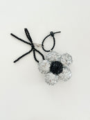 An silver sequined flower keychain with a black center displayed in white background.