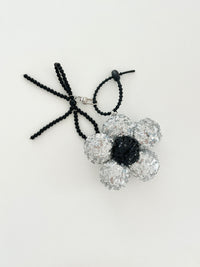 An silver sequined flower keychain with a black center displayed in white background.