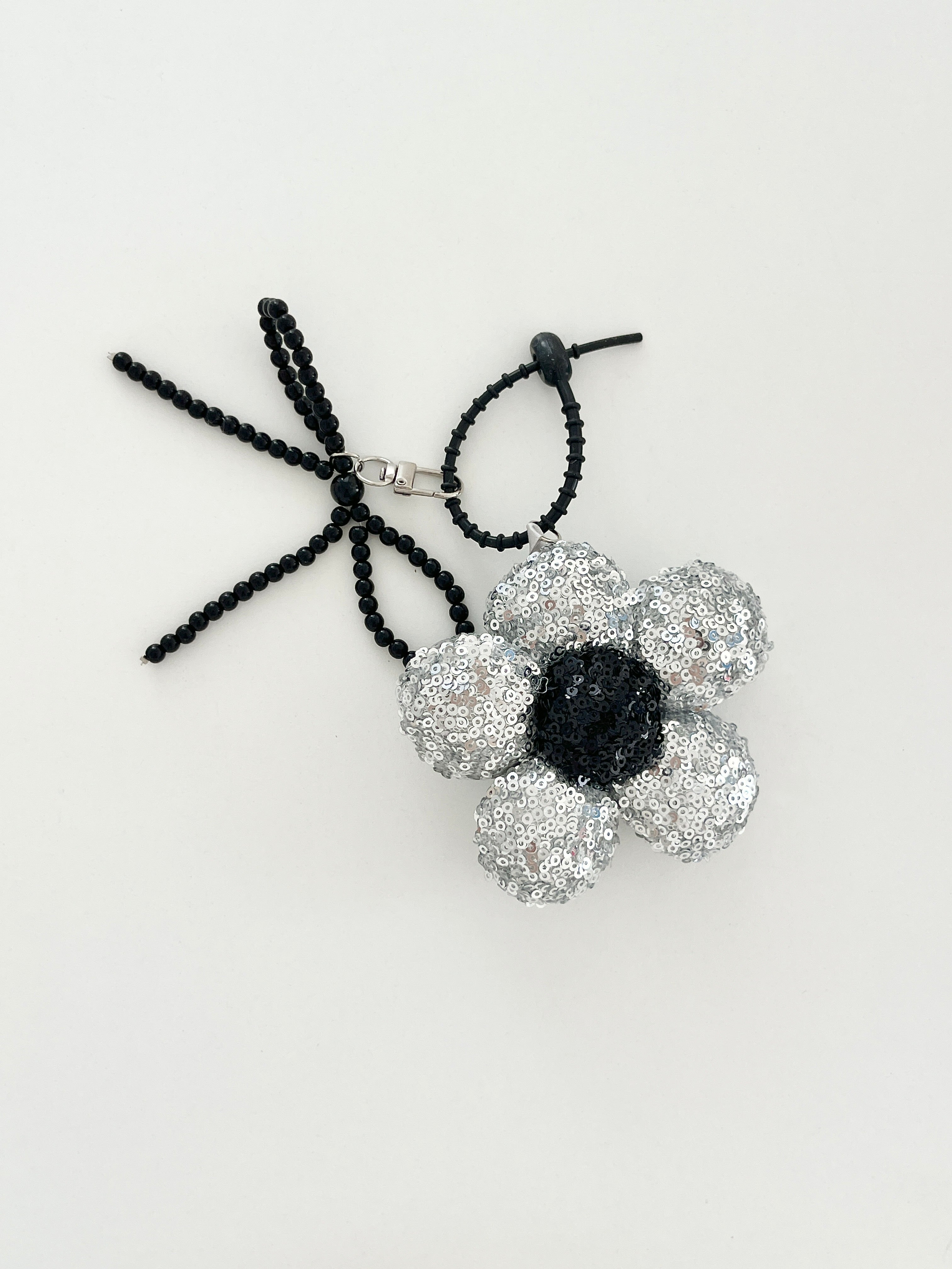 An silver sequined flower keychain with a black center displayed in white background.