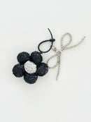 A black sequined flower keychain with a  silver center displayed in white background.