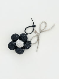 A black sequined flower keychain with a  silver center displayed in white background.