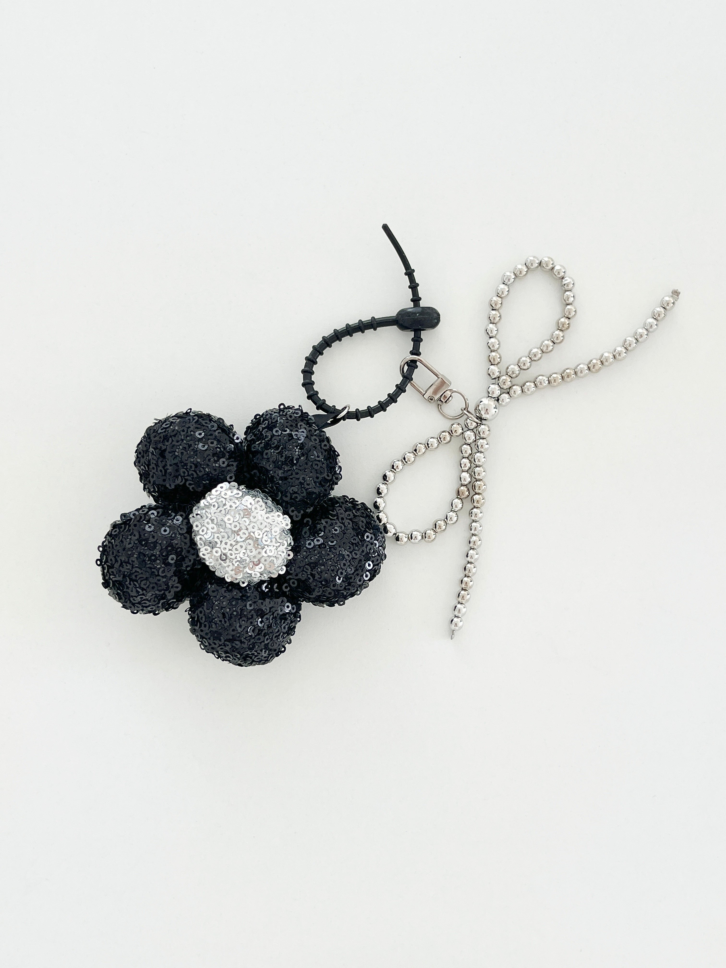 A black sequined flower keychain with a  silver center displayed in white background.