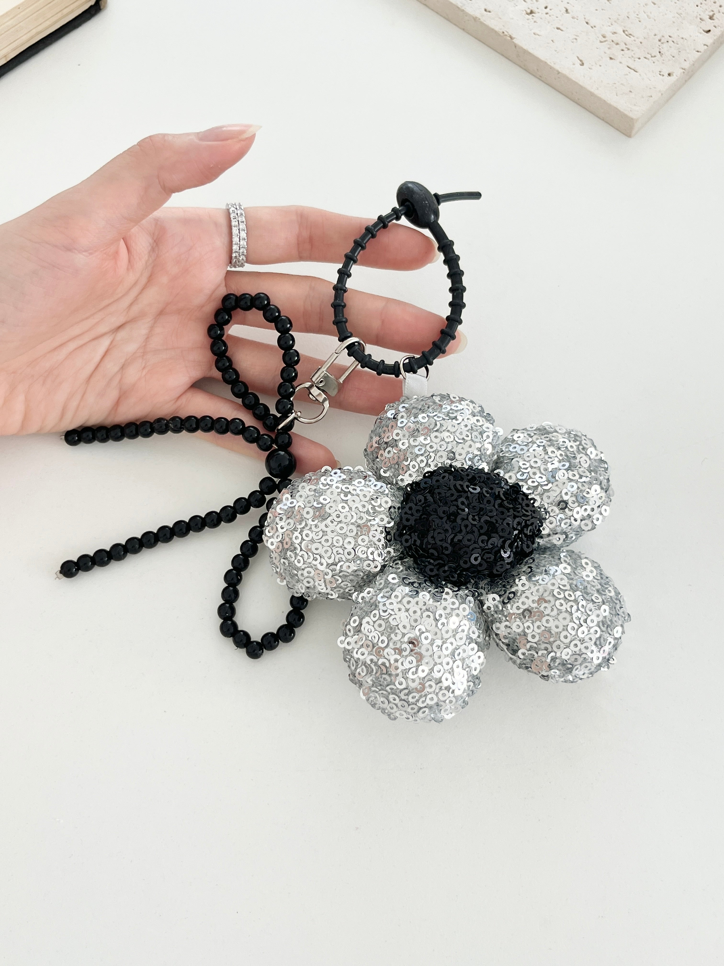 One silver sequined flower keychains, with a black center shown on a hand.