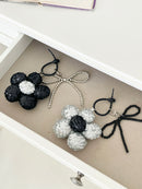 Two sequined flower keychains in black and silver with matching bead bow charms, neatly arranged in a drawer next to each other.