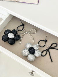 Two sequined flower keychains in black and silver with matching bead bow charms, neatly arranged in a drawer next to each other.