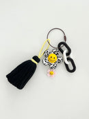 Black and white leopard print flower keychain with a yellow smiley face center, small yellow flower charm, and a black tassel hanging from chunky black and white links displayed in white background. 