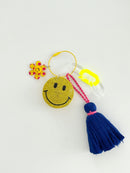 Colorful smiley face keychain with yellow rhinestone-covered charms, playful flower accents, and blue tassels, displayed on white surface.