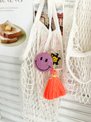 Colorful smiley face keychains with pink rhinestone-covered charms, playful flower accents, and  neon orange tassels, displayed on white surface hanging from a mesh bag.