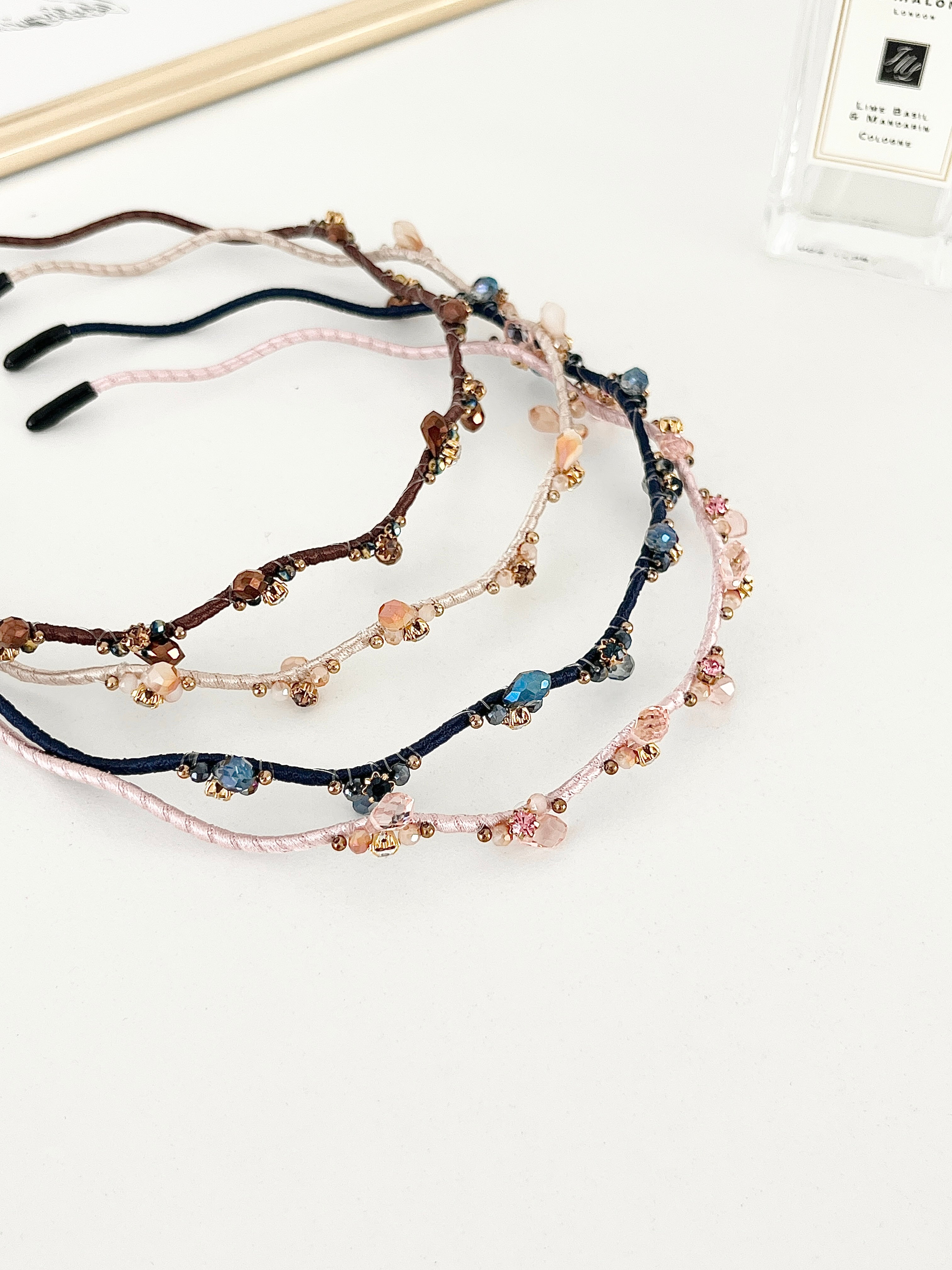 Four crystal hairbands displayed on white background in brown, beige, navy, and light pink. Each with branch-like designs and small crystals.