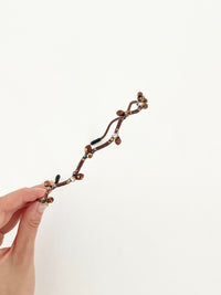 Hand holding a hairband with branch-like design and small crystal in brown color.