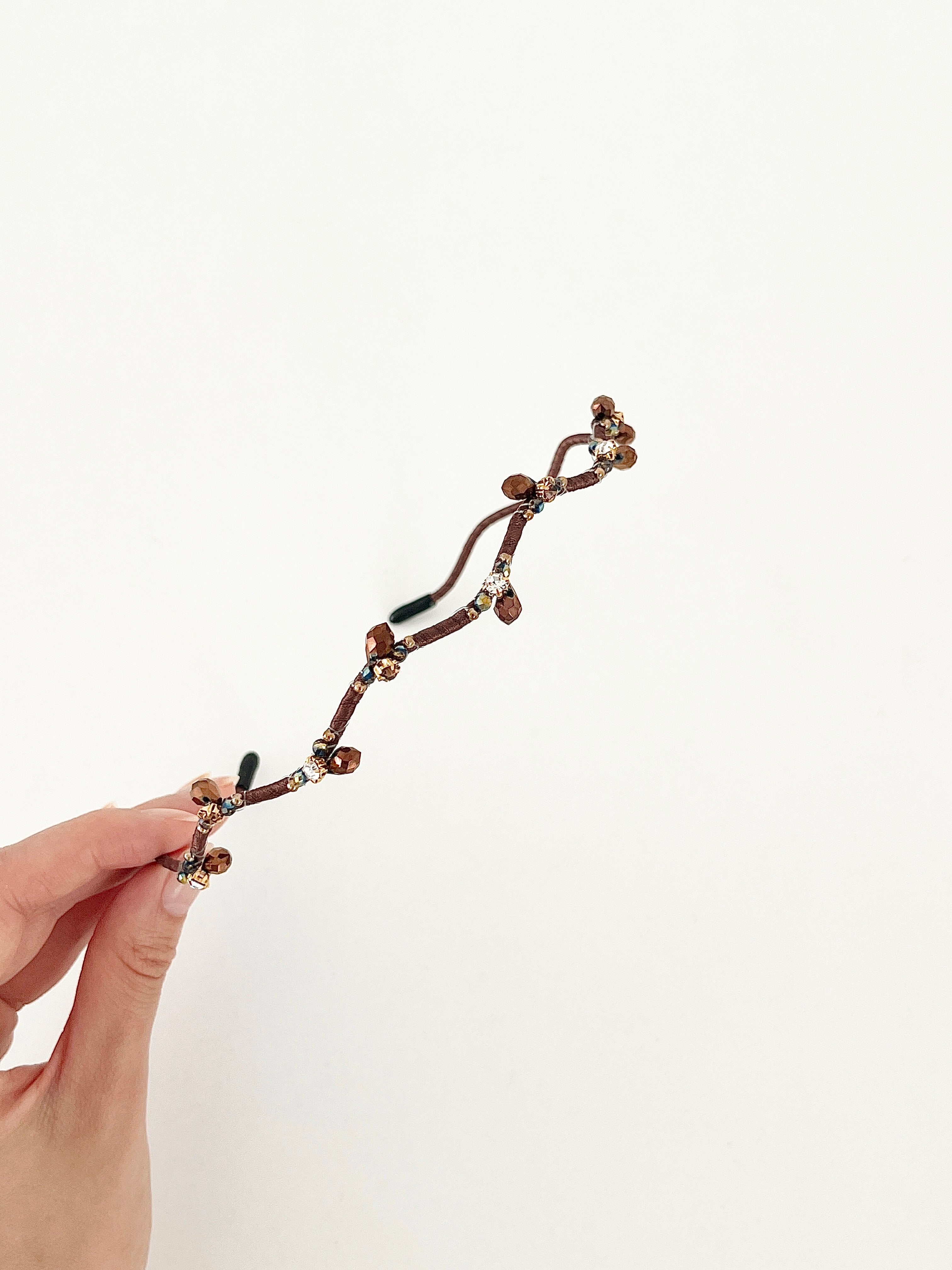 Hand holding a hairband with branch-like design and small crystal in brown color.