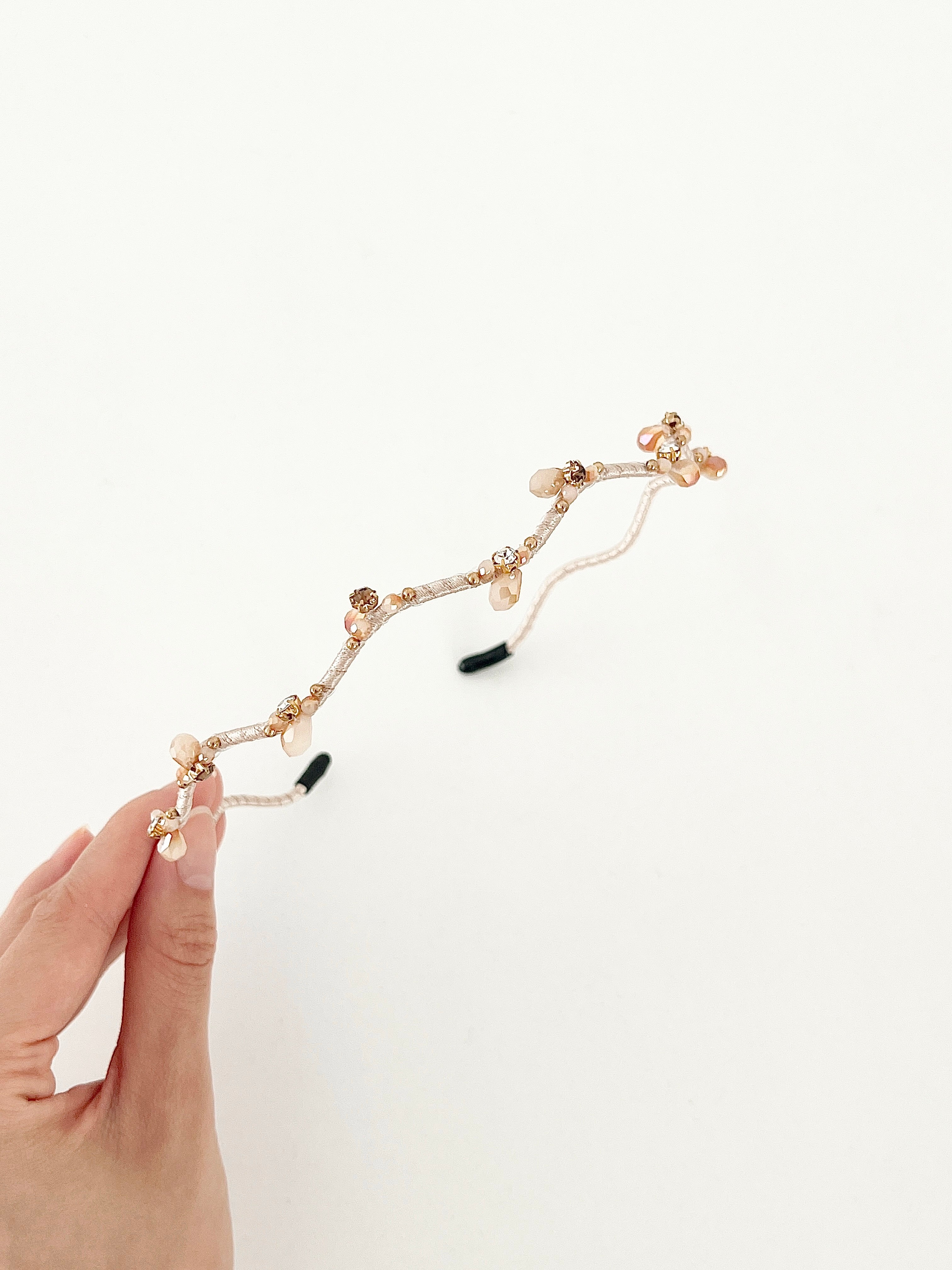 Hand holding a hairband with branch-like design and small crystal in beige color.