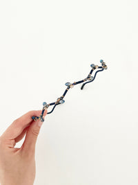 Hand holding a hairband with branch-like design and small crystal in navy color.