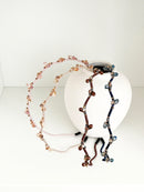 Four crystal hairbands in pale pink, beige, brown, and navy, each with branch-like designs and small crystals, displayed resting on a white round vase.